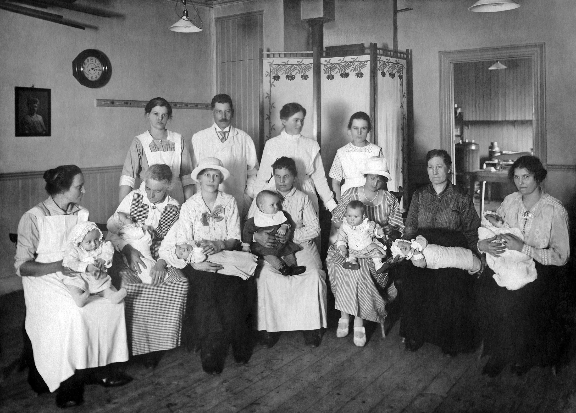 Sju kvinnor som sitter med varsitt spädbarn i famnen, år 1921. Bakom dem står tre kvinnor och en man.